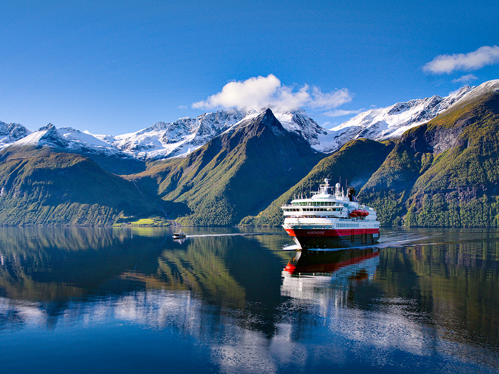 Hurtigruten sailing in a Norwegian fjord with snow capped mountains in the background