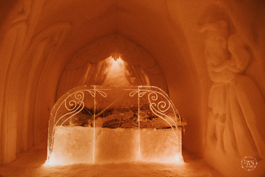 Carved Ice hotel suite in orange light with decorated bed end at Sorrisniva, Alta by Sorrisniva